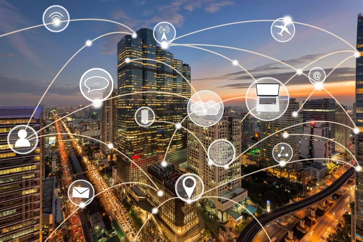 A cityscape at dusk with numerous skyscrapers connected by lines and various icons, symbolizing digital connectivity and the Internet of Things (IoT).